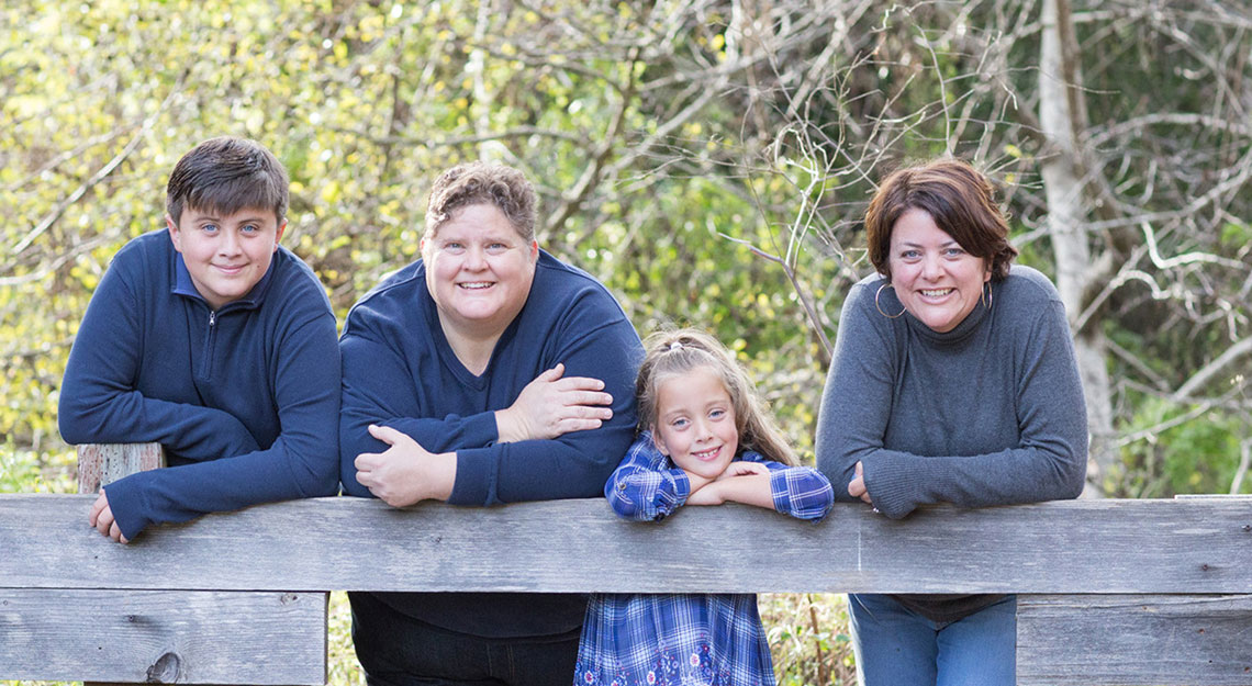 A family smiling, posing in front of a fence at a park